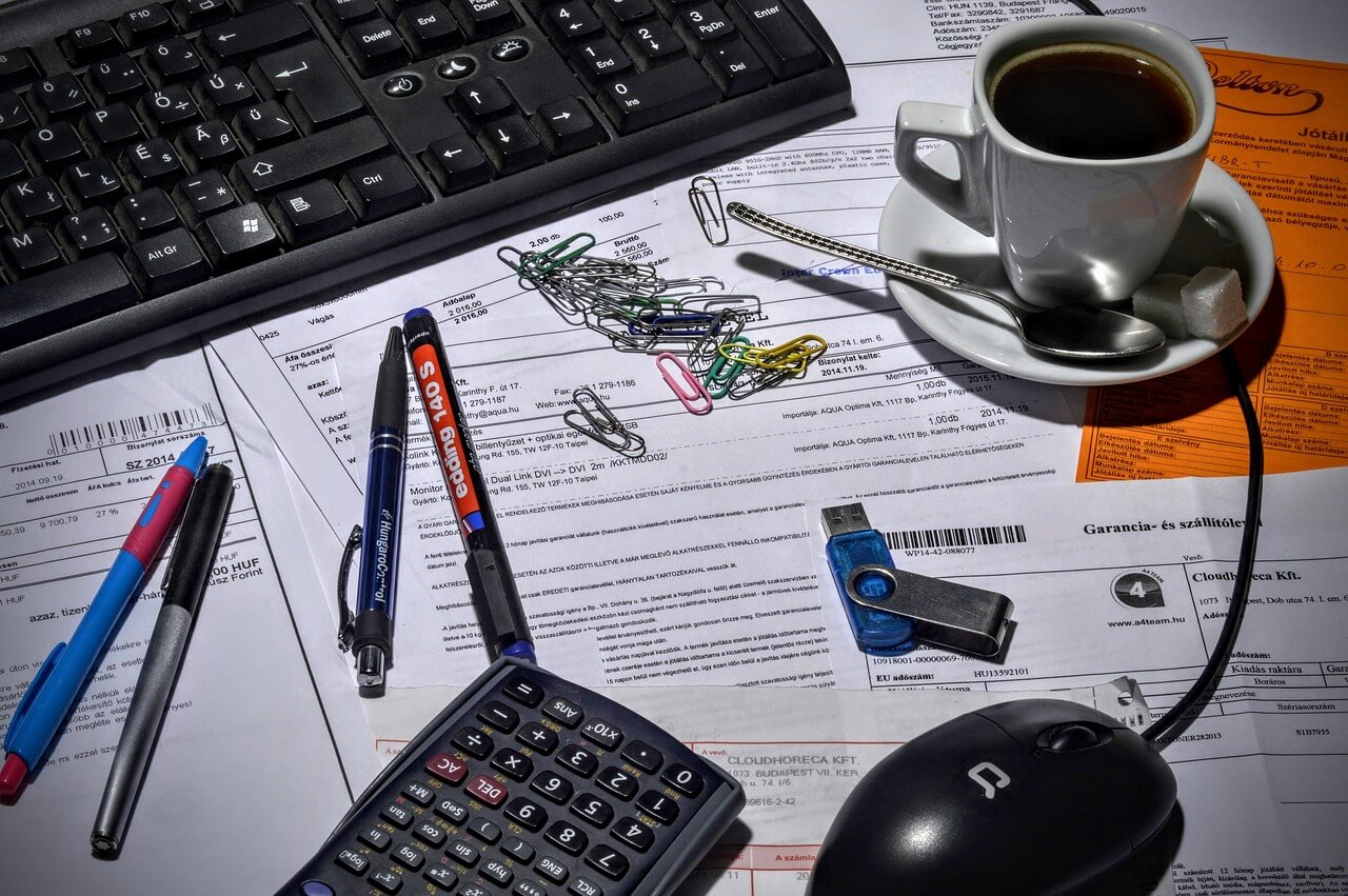 desk cluttered with keyboard pens coffee etc